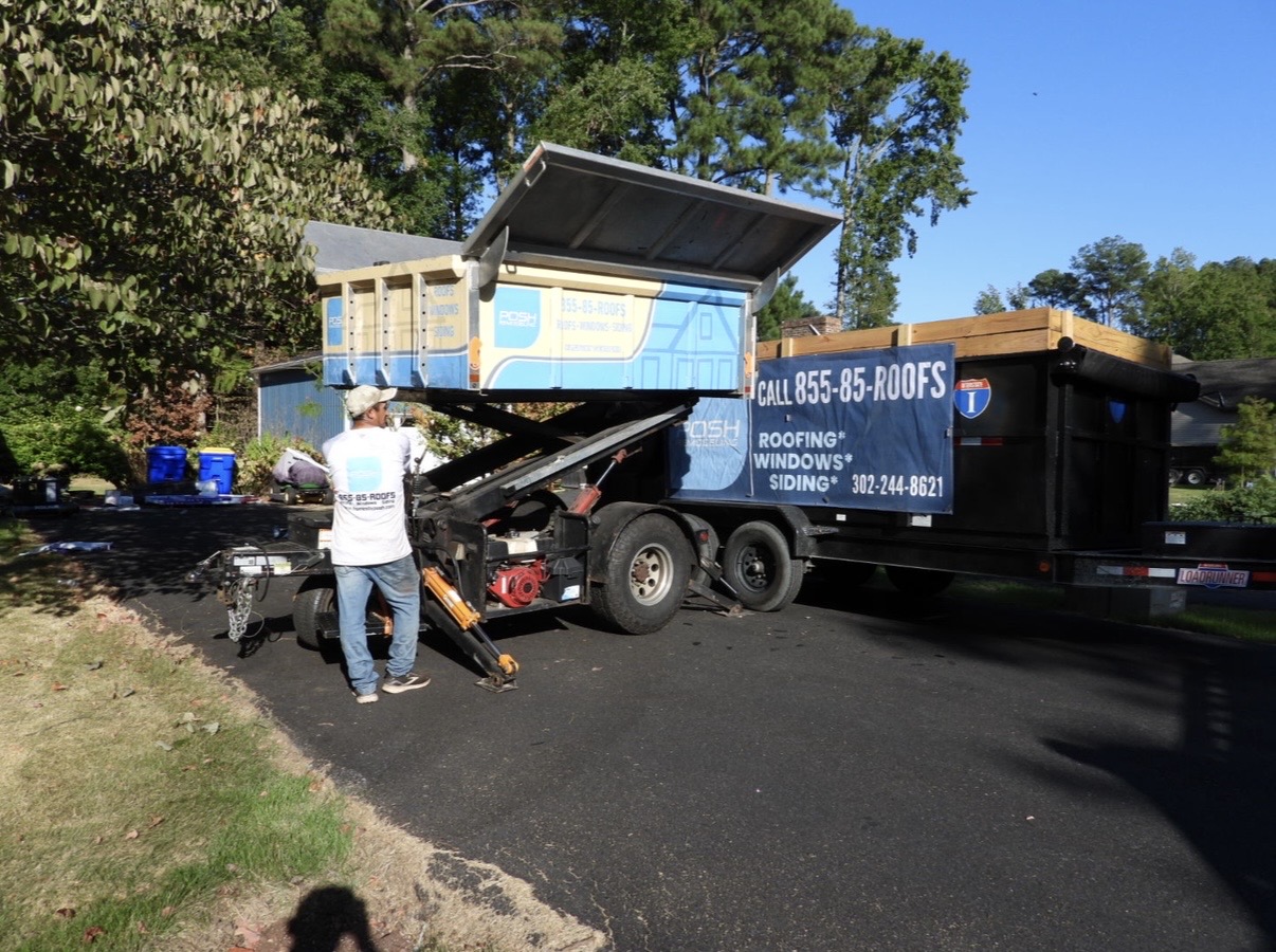 Roofing crew operating a debris lift beside a covered dump trailer